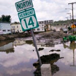 A small tractor clears water from a business as flood waters block a street.