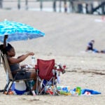 Sierra Payne, of Boston, reaches for a bottle of water while trying to stay cool under an umbrella as she visits Wollaston Beach.