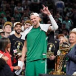 Boston Celtics center Kristaps Porzingis, center, raises his arm as he celebrates with teammates near the Larry O'Brien Championship Trophy after the Celtics won the NBA championship with a Game 5 victory over the Dallas Mavericks on Monday, June 17, 2024, in Boston.