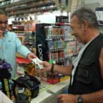 A man purchases a lottery ticket from another man inside a convenience store